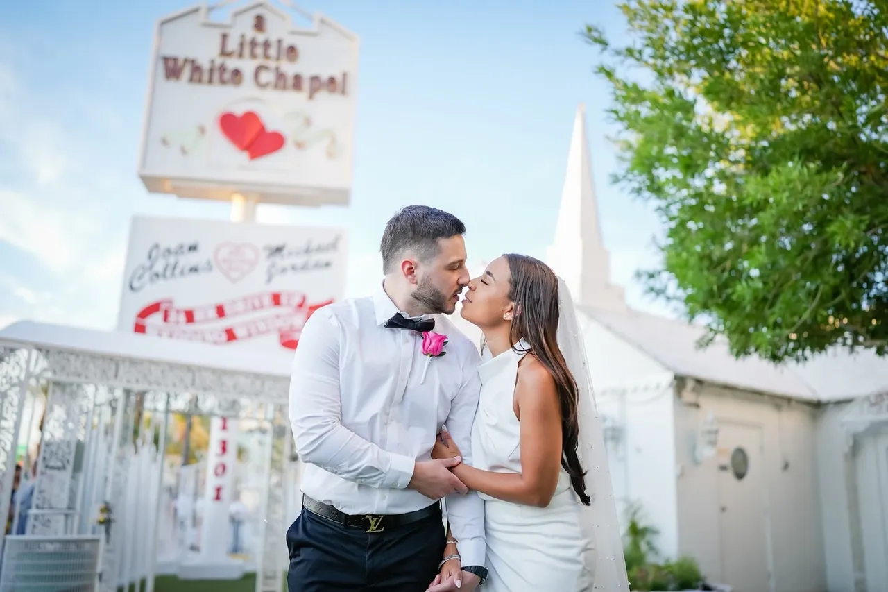 A man and woman kissing in front of a little white chapel sign.