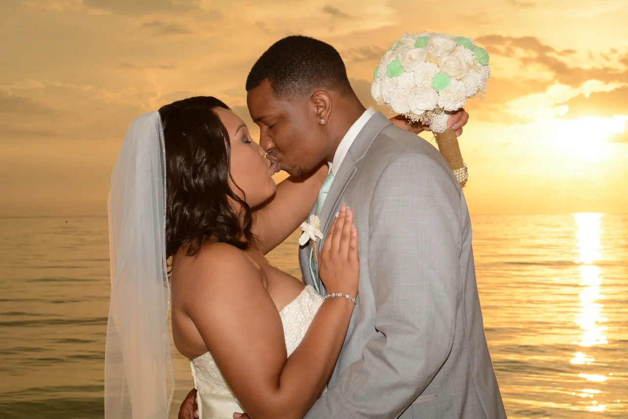 A bride and groom kissing at sunset on the beach.