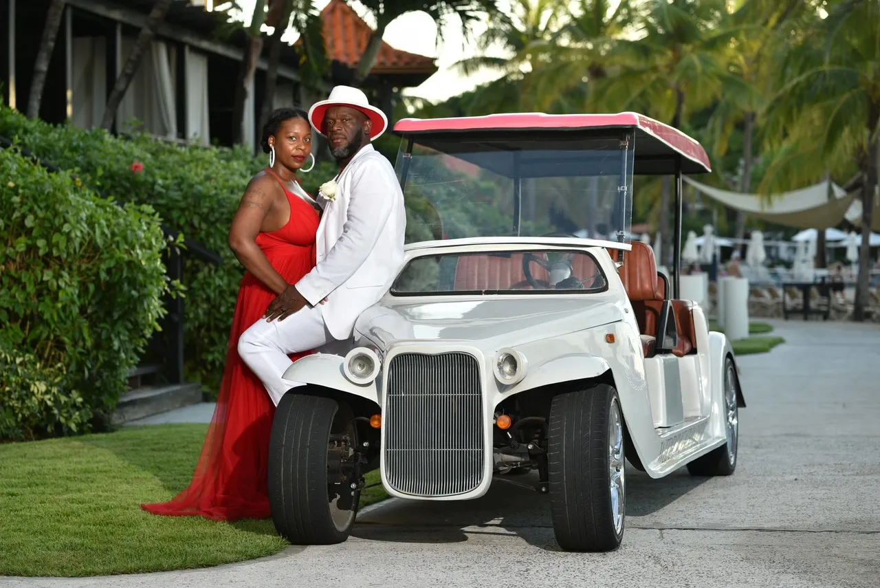 A man and woman posing in front of an old fashioned golf cart.