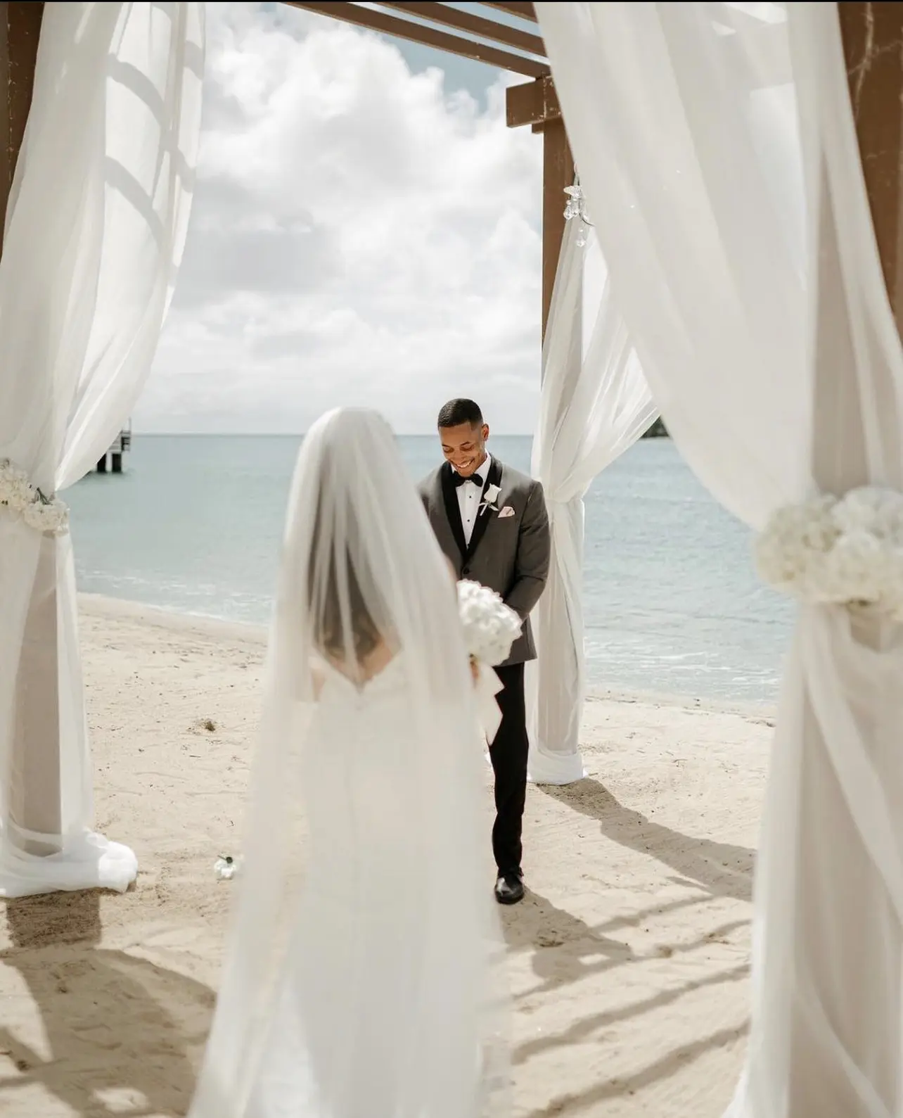 A bride and groom standing under an awning on the beach.