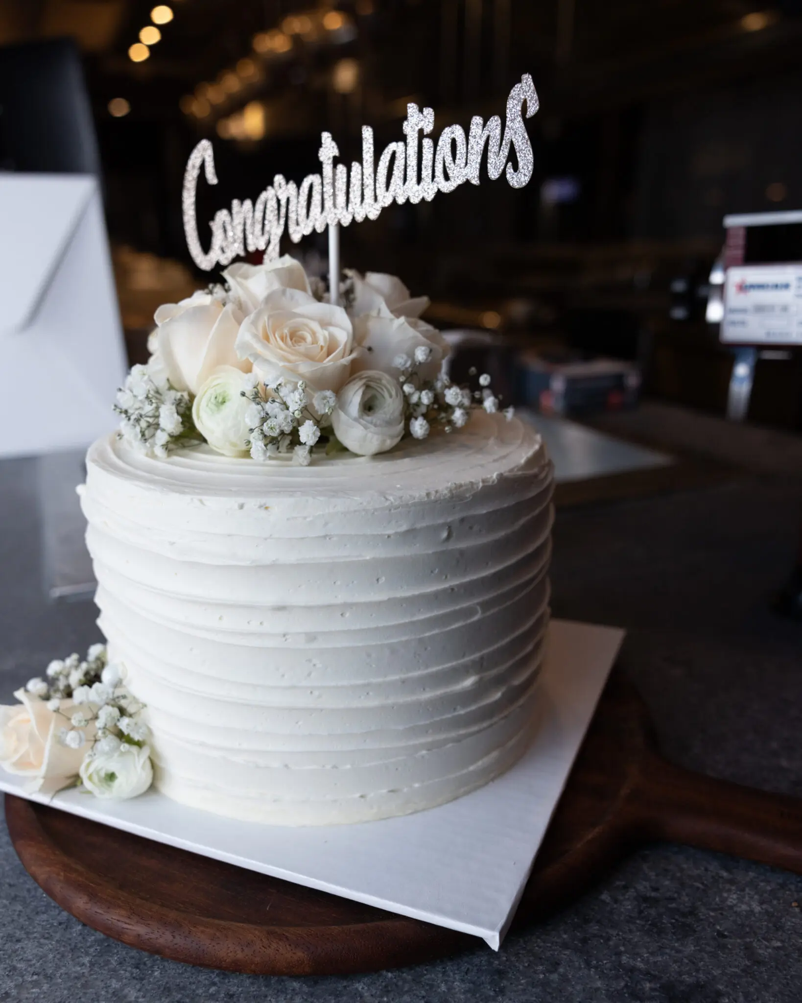 White cake with flowers and "congratulations" topper.