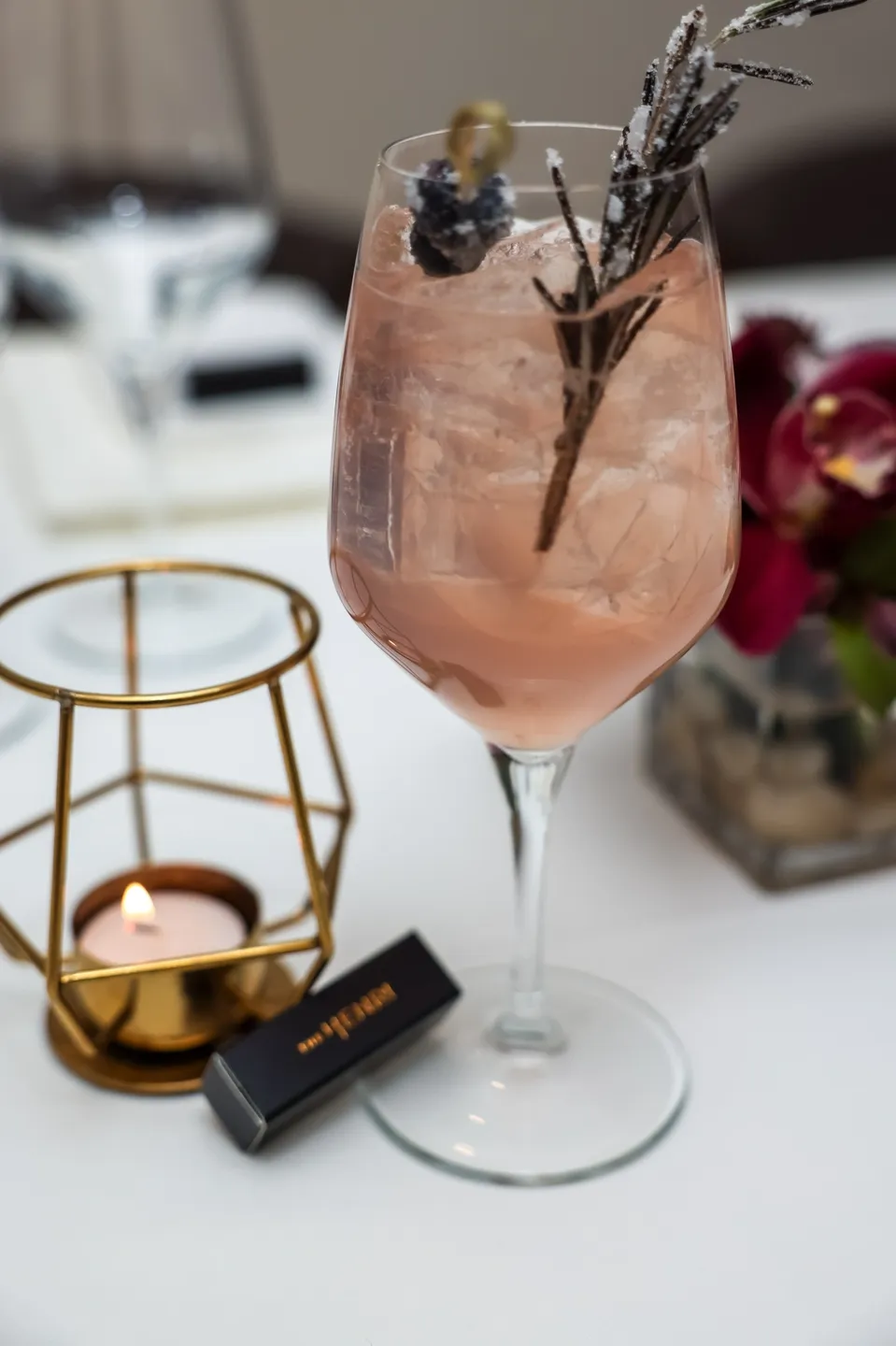 Pink cocktail with rosemary garnish in glass.