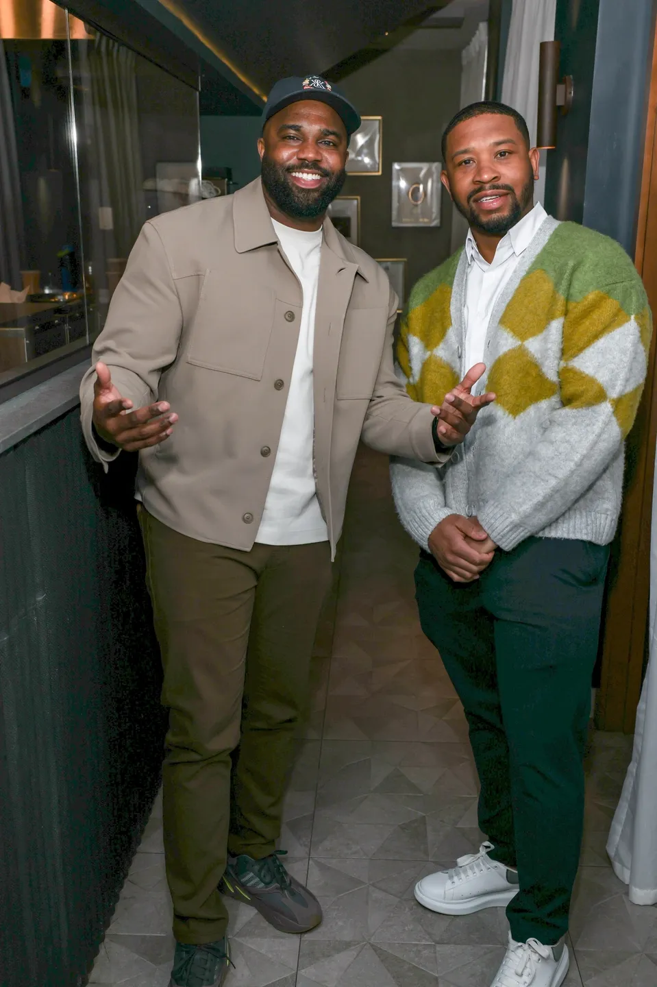 Two men smiling, one in a beige jacket.