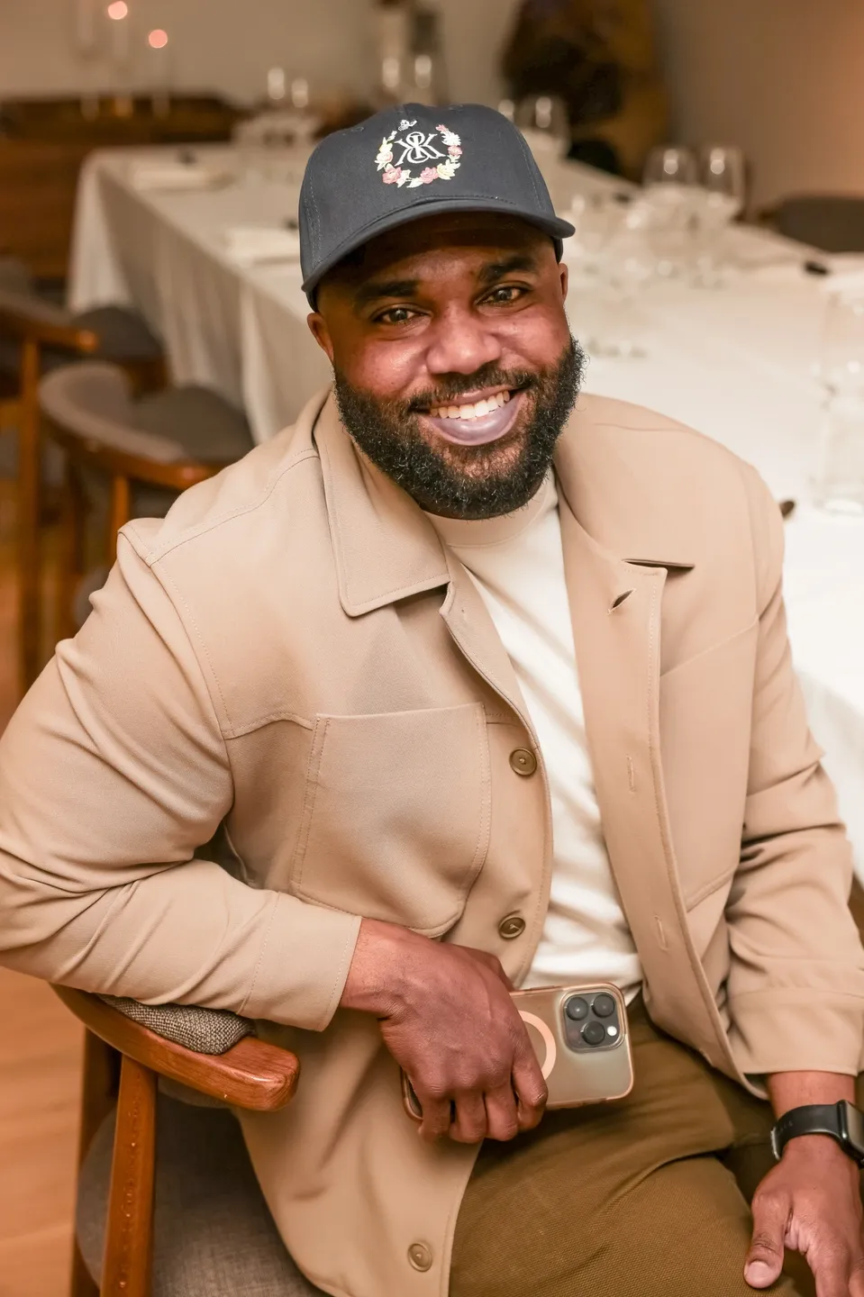 Man in tan jacket and black hat smiling.