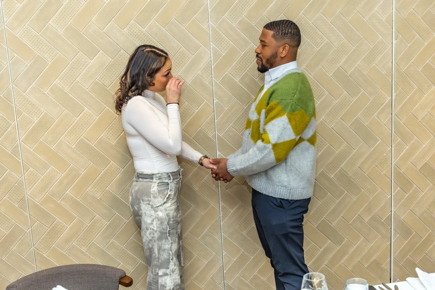 Couple holding hands in front of tiled wall.