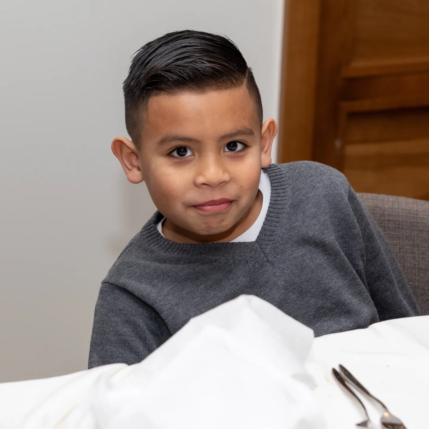 Young boy in grey sweater smiling at camera.