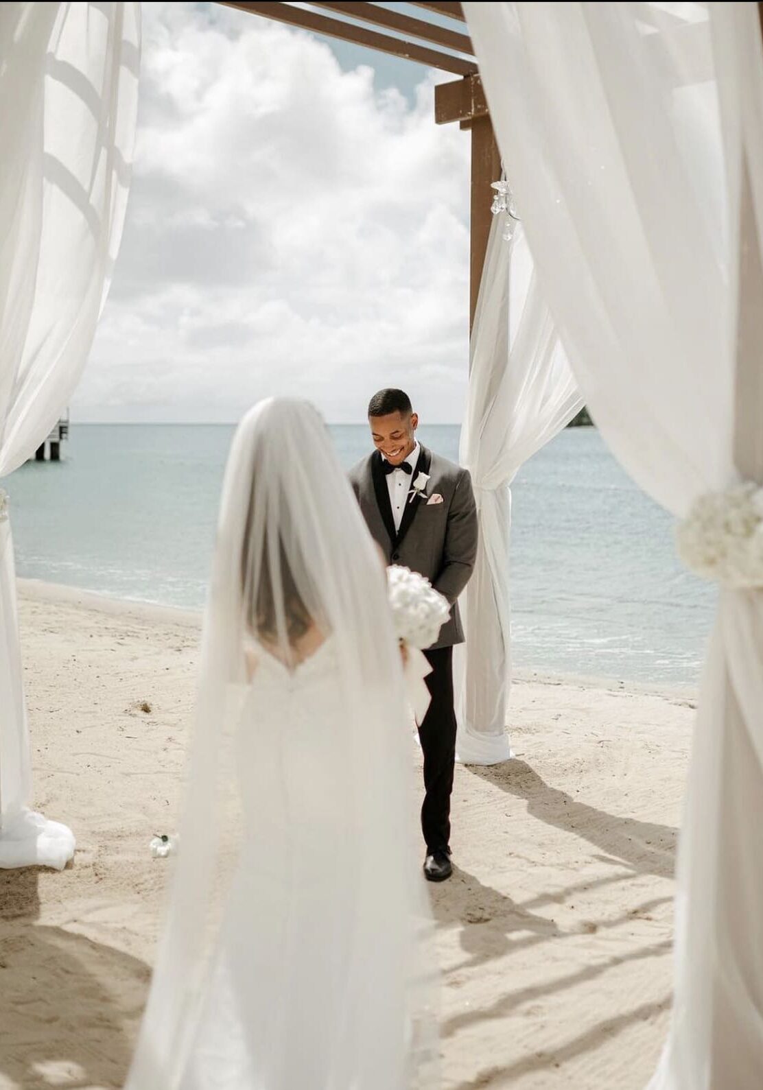 A bride and groom standing under an awning on the beach.